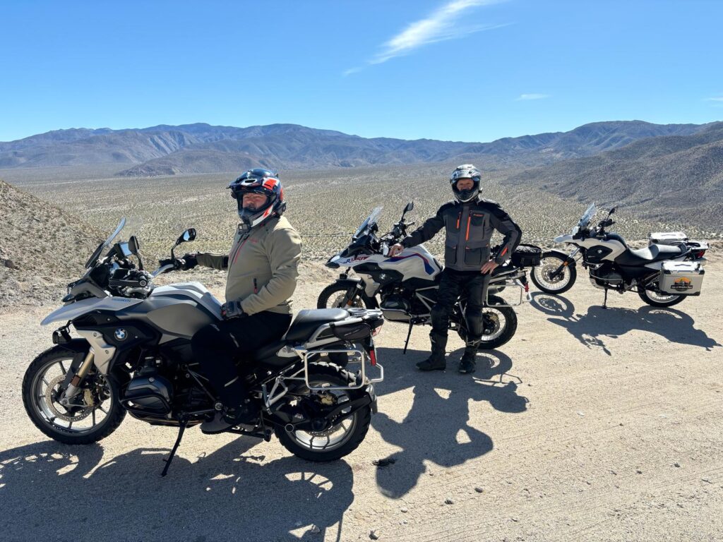 Two motorcycle riders stand next to three BMW adventure motorcycles overlooking the Anza Borrego Desert State Park outside of San Diego, CA