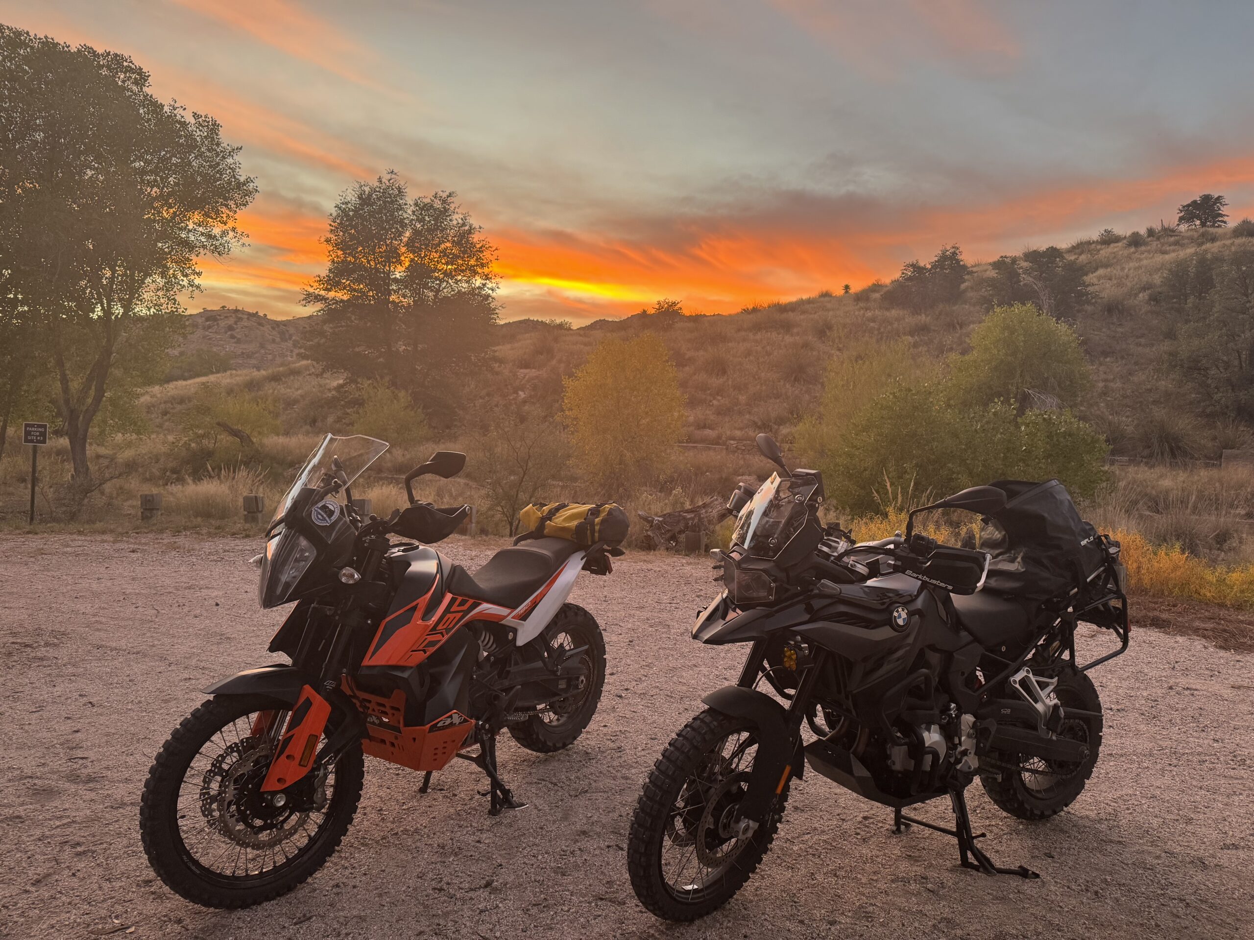 A KTM 790 Adventure and BMW F850GS adventure motorcycle are situated in front of a brilliant orange sunset in the Arizona desert near Tucson