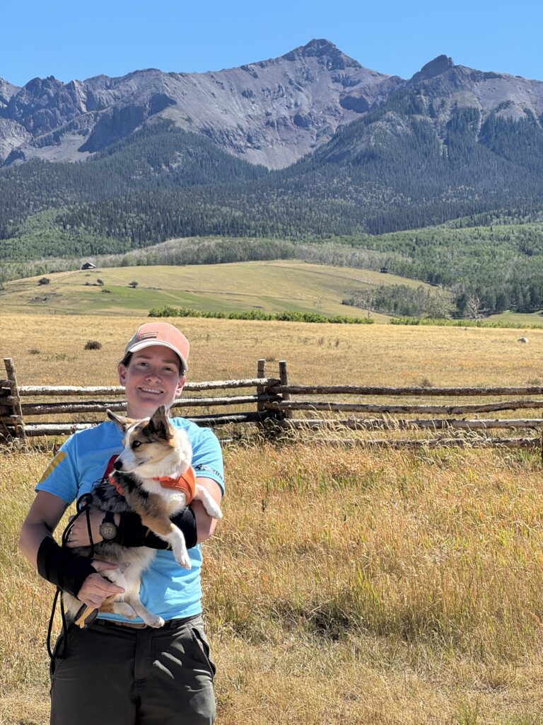 Caitlin and her dog, Churro, stand with the Mount Sneffels area of the San Juan mountains in the background.