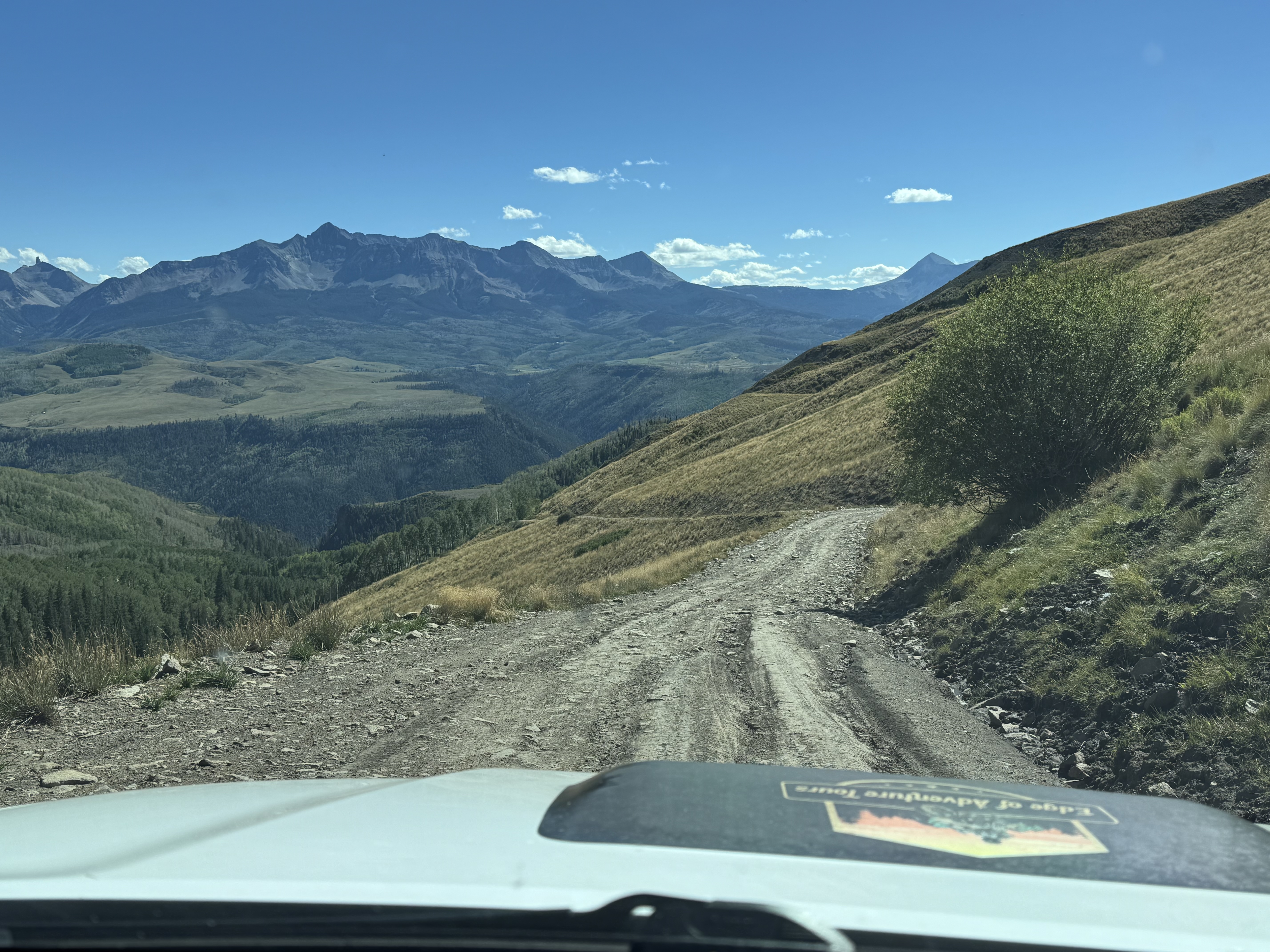 A logo on the hood scoop of a Toyota 4runner on an offroad trail with the San Juan mountains of Colorado in the background.